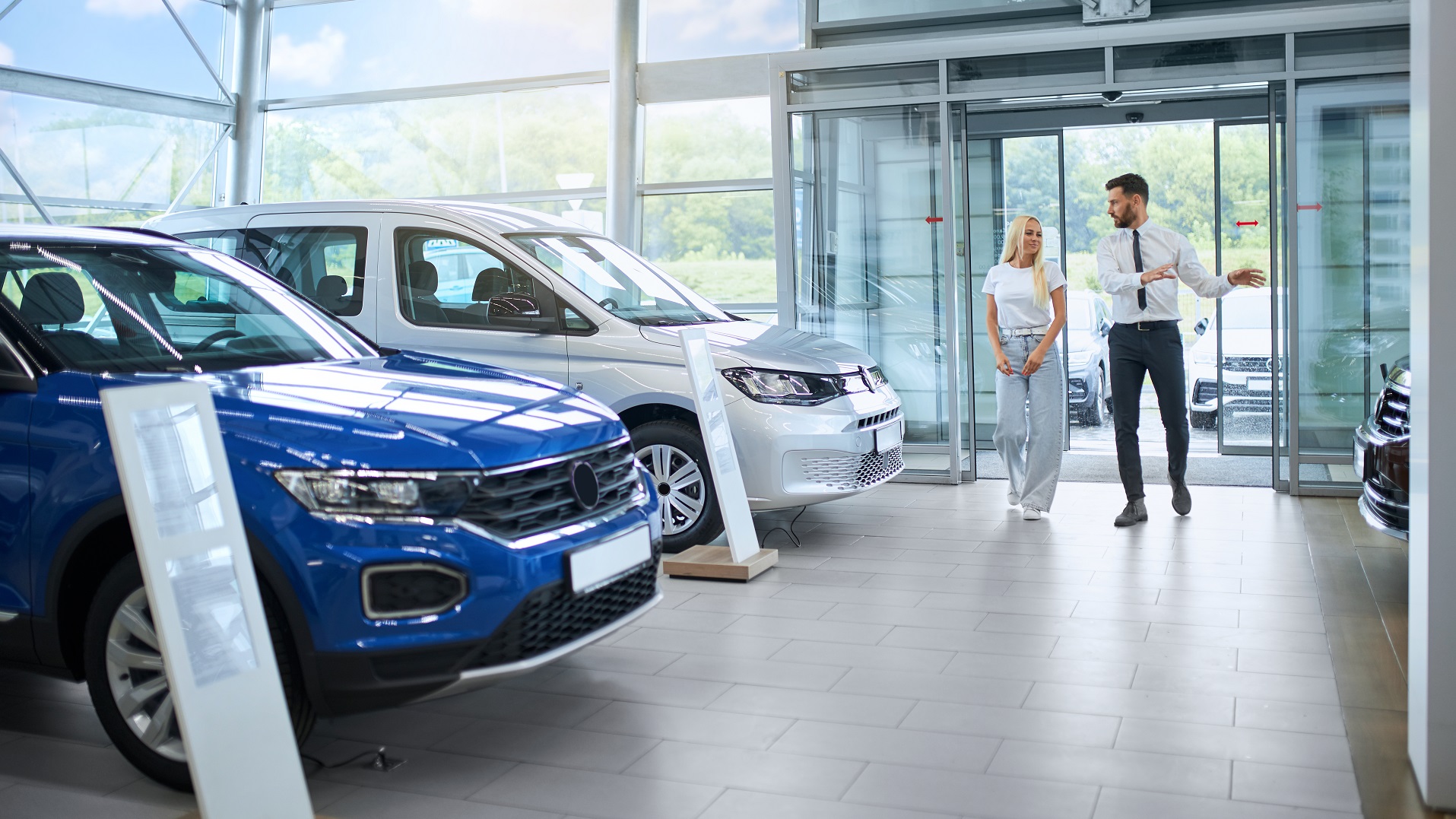 Salesman showing various cars to female client at shop